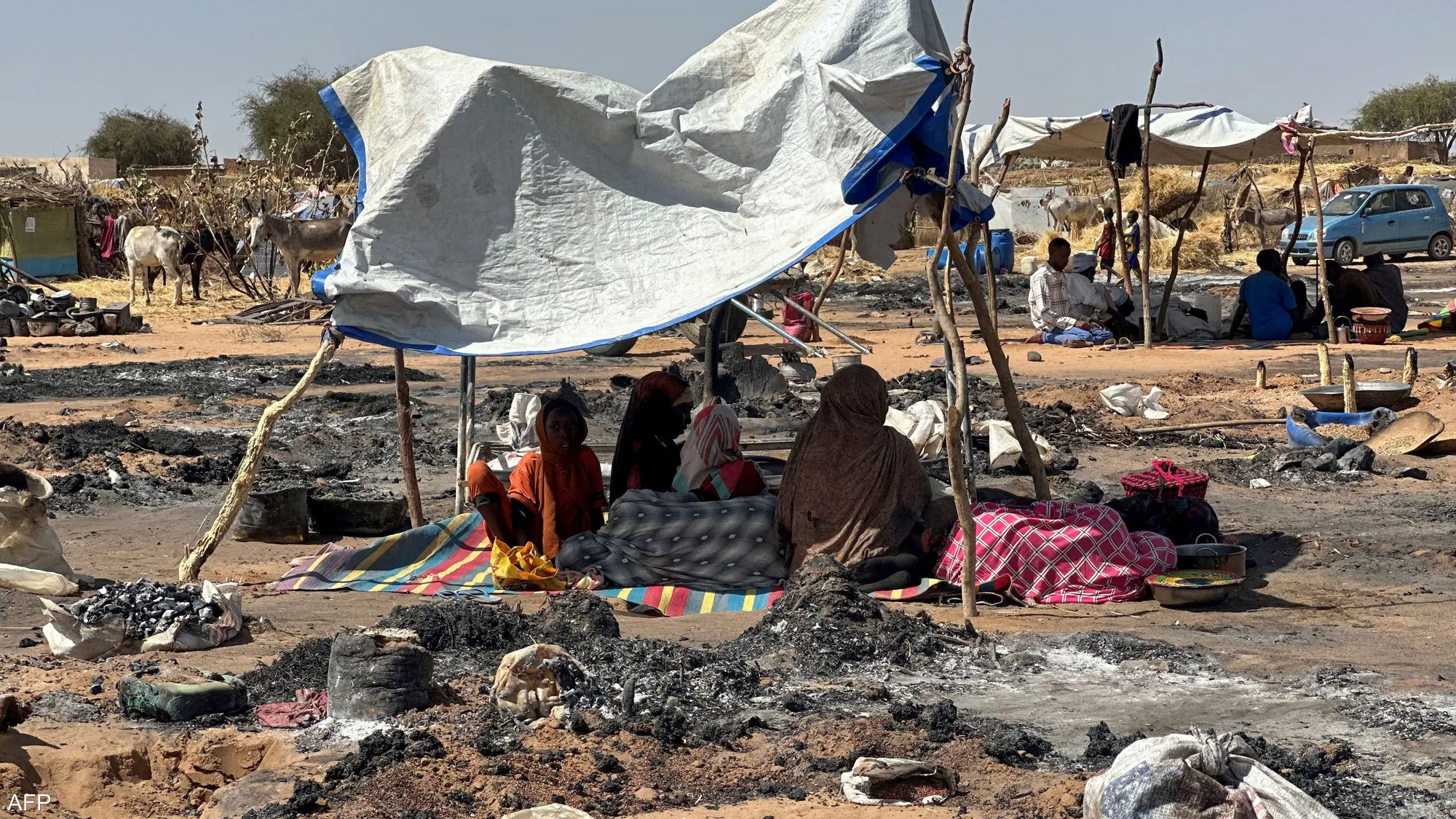 Displaced Sudanese families sit beside their belongings at a temporary shelter site after fleeing violence in Sudan's ongoing conflict.