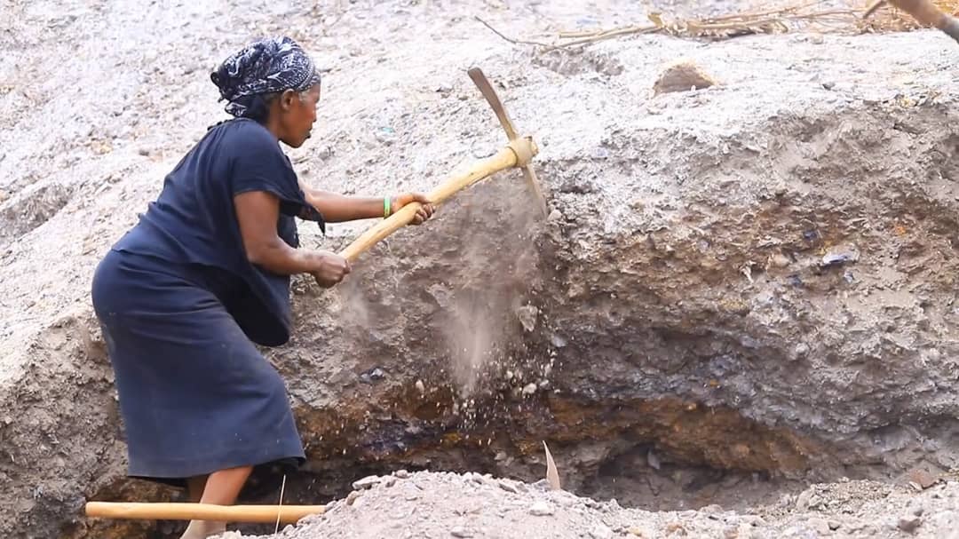 A woman strikes the ground as she digs for mineral ore at a mining site in Kisoro District, southwestern Uganda.