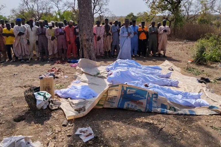 People pray beside the bodies of victims of an attack by gunmen before their burial in the Woro community in Nigeria's Kwara State on February 4, 2026 [Oluseyi Dasilva/Reuters]