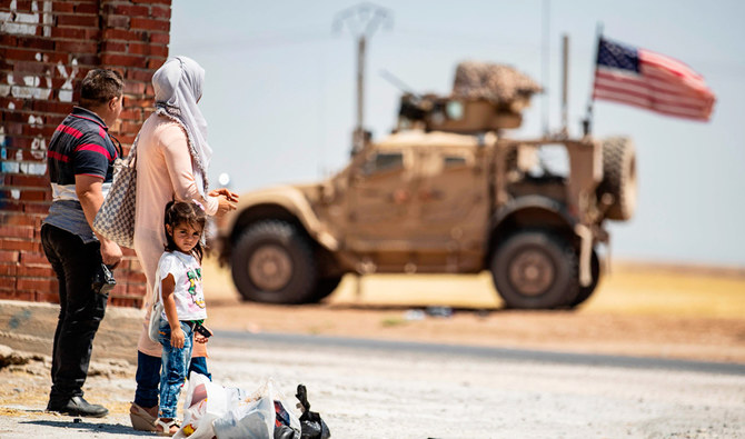A family stands across a US military vehicle parked on the outskirts of Rumaylan in Syria's northeastern Hasakeh province. (AFP)