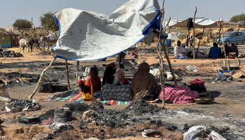 Displaced Sudanese families sit beside their belongings at a temporary shelter site after fleeing violence in Sudan's ongoing conflict.