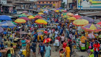 Traders and customers navigate busy market stalls in Nigeria, where easing inflation has yet to significantly reduce the high cost of everyday food and essential goods.