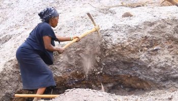A woman strikes the ground as she digs for mineral ore at a mining site in Kisoro District, southwestern Uganda.