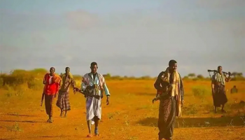 Armed Somali men move through rural terrain.