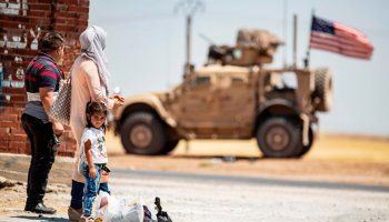 A family stands across a US military vehicle parked on the outskirts of Rumaylan in Syria's northeastern Hasakeh province. (AFP)
